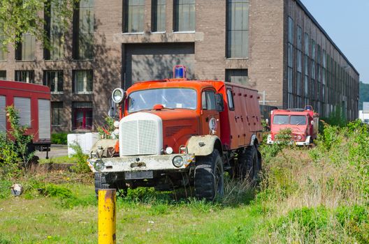 Old abandoned fire truck on a meadow in front of an old factory building.
