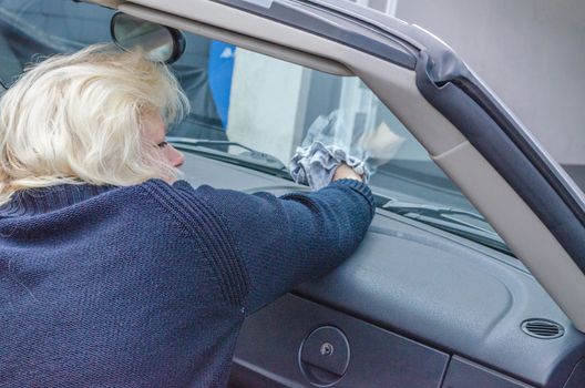 Woman with blond hair cleans the windshield of a convertible.
