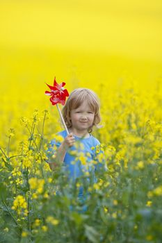 boy with long blond hair holding pinwheel in canola field