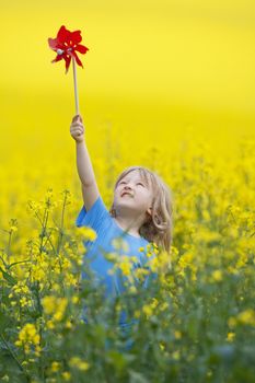 boy with long blond hair holding pinwheel in canola field