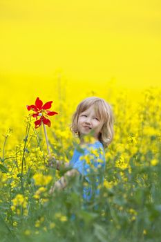 boy with long blond hair holding pinwheel in canola field