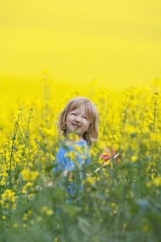 boy with long blond hair holding pinwheel in canola field