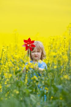 boy with long blond hair holding pinwheel in canola field