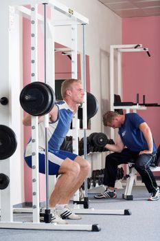 young man lifting heavy bar-bell in modern gym