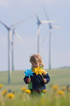 boy with long hair holding pinwheels standing in front of wind turbines