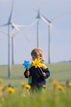 boy with long hair holding pinwheels standing in front of wind turbines