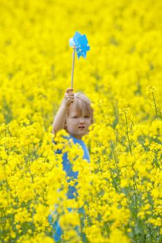 boy with long blond hair holding pinwheel in canola field