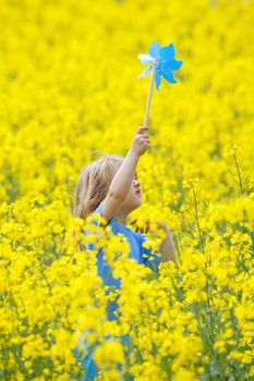 boy with long blond hair holding pinwheel in canola field