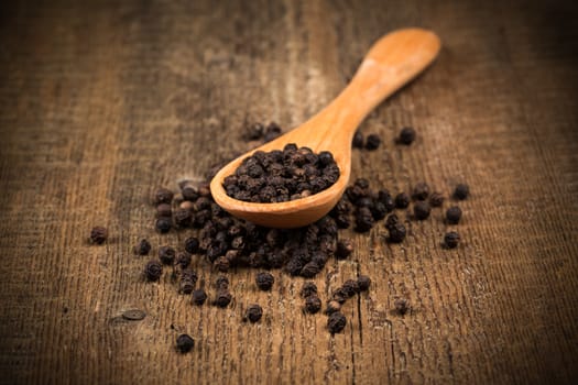 black pepper on wooden spoon and wood background