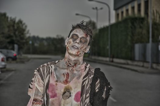 One male zombie standing in empty city street at night looking at camera. Halloween theme