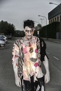 One male zombie standing in empty city street at night looking at camera. Halloween theme