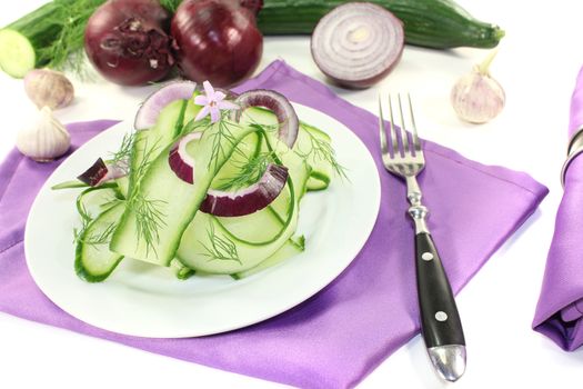 Cucumber salad with red onions, garlic flower and dill on light background