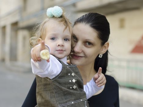 My mother is in the hands of the girl. The girl pointed forward and looking forward. My mother also looks into the camera. Street layout.