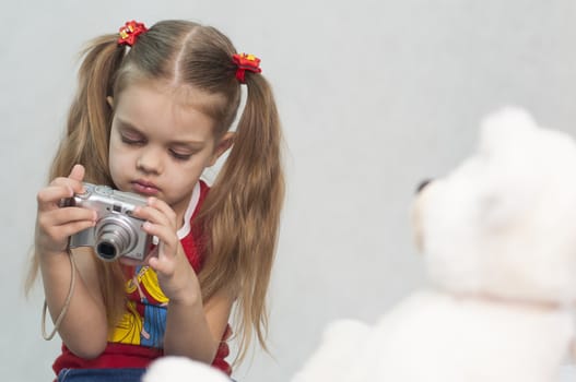 Girl playing in the photographer. Girl takes photo of Teddy digital camera and compares the result with the original