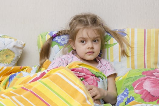 Four-year-old girl with pigtails and down the stairs. Pillow put to the wall and covered her bright blanket. Home furnishings.