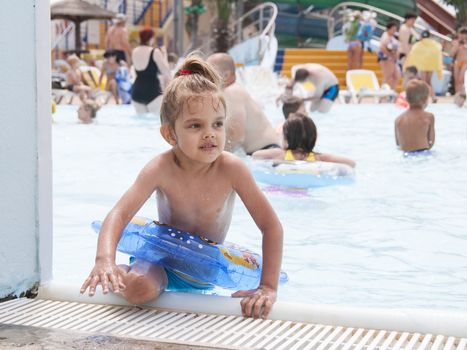 Four-year-old girl bathes in a public pool. Getting out of the pool with a put on yourself around. Summer day.