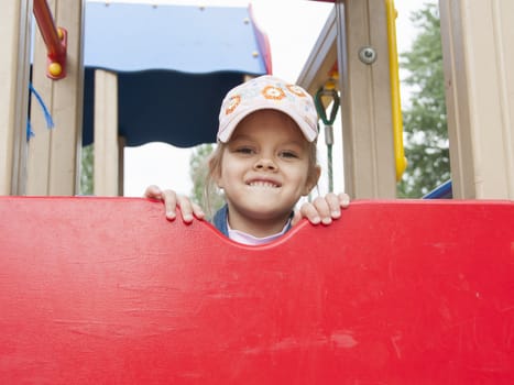 A girl peeks out from the top of the shield, while on the Playground. The girl is wearing a cap.