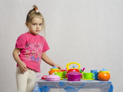 Girl plays child kitchen utensils. The girl is left of the table and looks in the frame