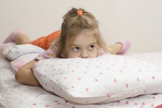 girl is lying on the bed. Buried her face in the pillow girl enthusiastically looking right. Home furnishings