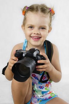 A merry girl keeps SLR camera. child rejoices, for the first time entrusted to hold the camera. The white background