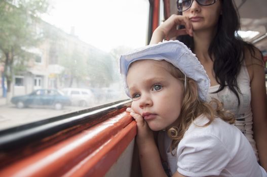 Little girl and mom goes to tram. Girl tired, thoughtfully, looking out the window.