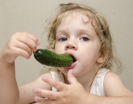 The girl sitting at the kitchen table and funny eating cucumber