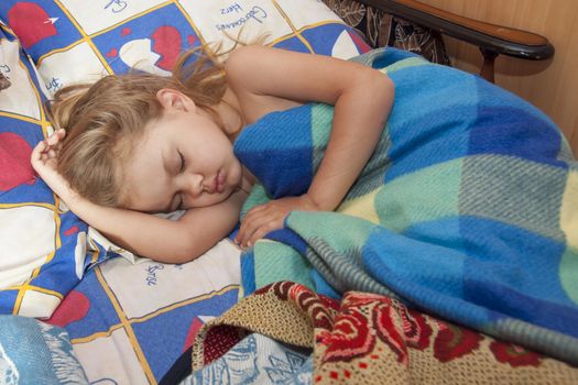 A child of four years old sleeps in the old bed adult. Girl covered with old blanket, rug old towels. Country variant of the beds.