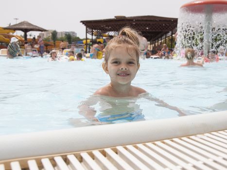 Four-year-old girl bathes in a public pool. The girl came up to the edge of the pool and looks into the frame. Summer day.l