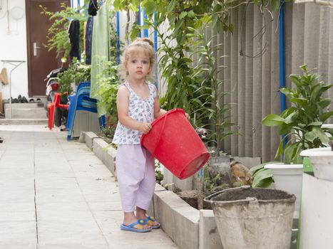 Girl stands in the yard of about watering the crane. The girl holding the bucket in his hands, and looks in the frame
