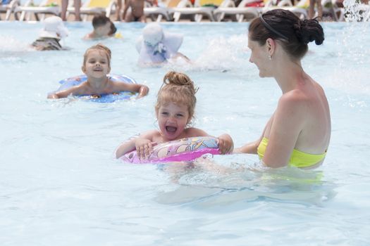A mother and two daughters are swimming in a public pool. Daughters of the two and four years. Daughter swim in circles