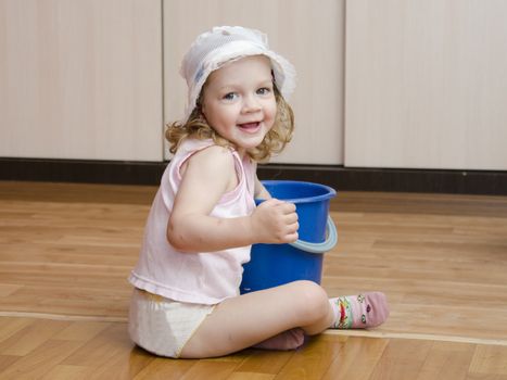 Two-year-old girl with pleasure and fun washing the floors in the room. Nearby is a small blue bucket