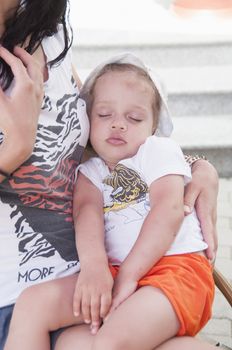 Little girl in shorts and a t-shirt fell asleep at hands of the mother in a warm summer day