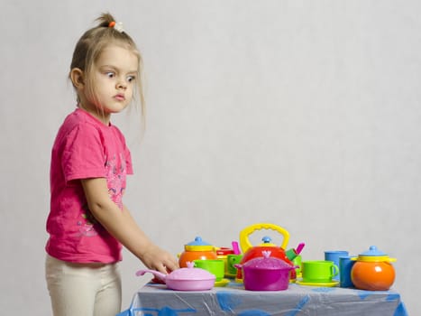 Girl plays child kitchen utensils. The girl is left of the table and looks in the frame