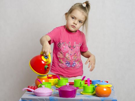 Girl plays child kitchen utensils. She picked up the teapot and poured a schematic of the water from the kettle into the Cup.