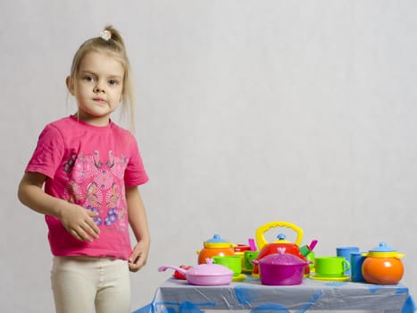 Girl plays child kitchen utensils. The girl is left of the table and looks in the frame