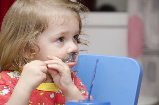 girl eats a cake sitting at the table. Passionately licks spoon and looks right. Home furnishings