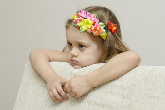 The girl thoughtfully looks to the left, his arms dangling from the back of the couch, and laid on the sofa his head. On the head of a girls band with beautiful flowers