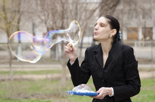 A girl inflates a big bubble. Street, early spring
