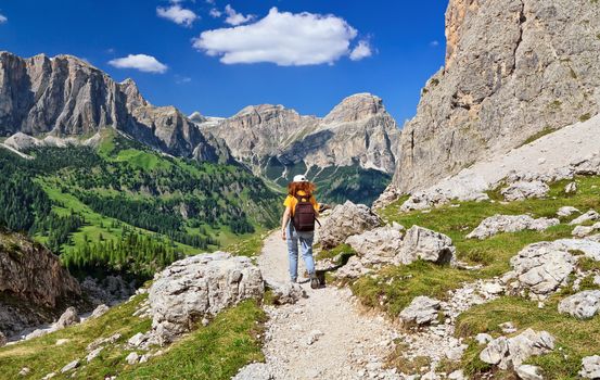 hiker on footpath  in Sella mountain, on background Colfosco and Badia Valley, south Tyrol, Italy