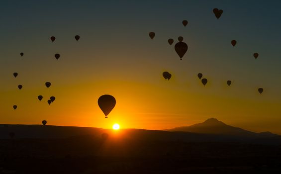 Silhouetts of hot balloons in morning sunrise and a mountain Erciyes. Cappadocia, Turkey