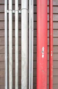 Red and silver pipe of plumbing system on brown wall.