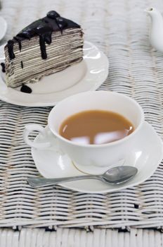 A cup of tea with chocolate crape cake on weave texture table