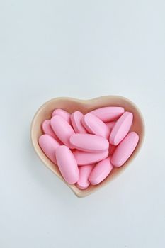 Many pink oval pills in the ceramic cup shape of heart.