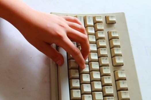 The childs hand on old computer keyboard.
