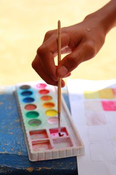 The hand holding the paintbrush to mix color for painting.