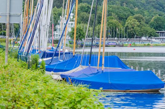 Sailboats under a blue cover with a tarpaulin at berth in port.