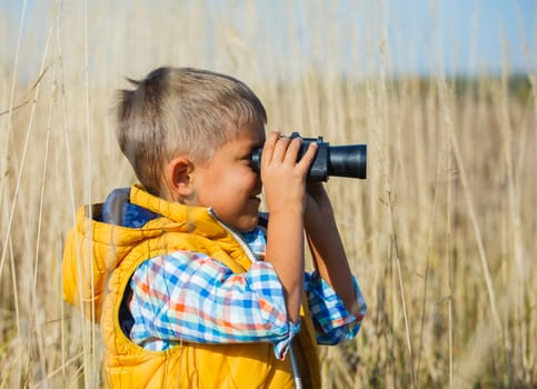 Young boy child playing pretend explorer adventure safari game outdoors with binoculars and bush hat