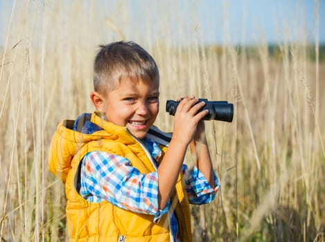 Young boy child playing pretend explorer adventure safari game outdoors with binoculars and bush hat