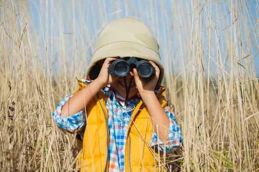 Young boy child playing pretend explorer adventure safari game outdoors with binoculars and bush hat