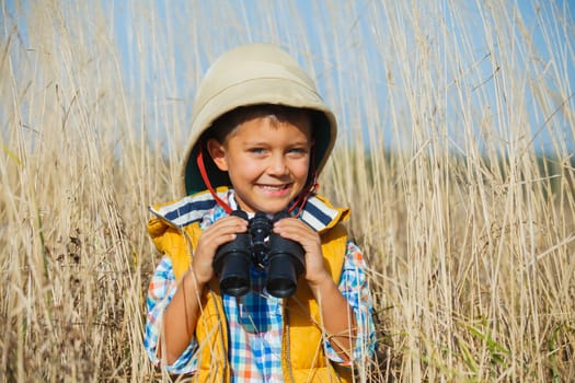 Young boy child playing pretend explorer adventure safari game outdoors with binoculars and bush hat